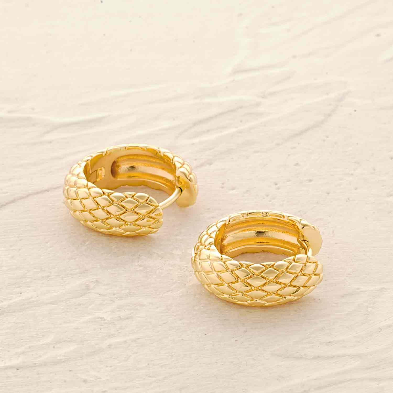 Close-up of chunky snakeskin huggie hoop earrings showing gold finish and textured snakeskin design