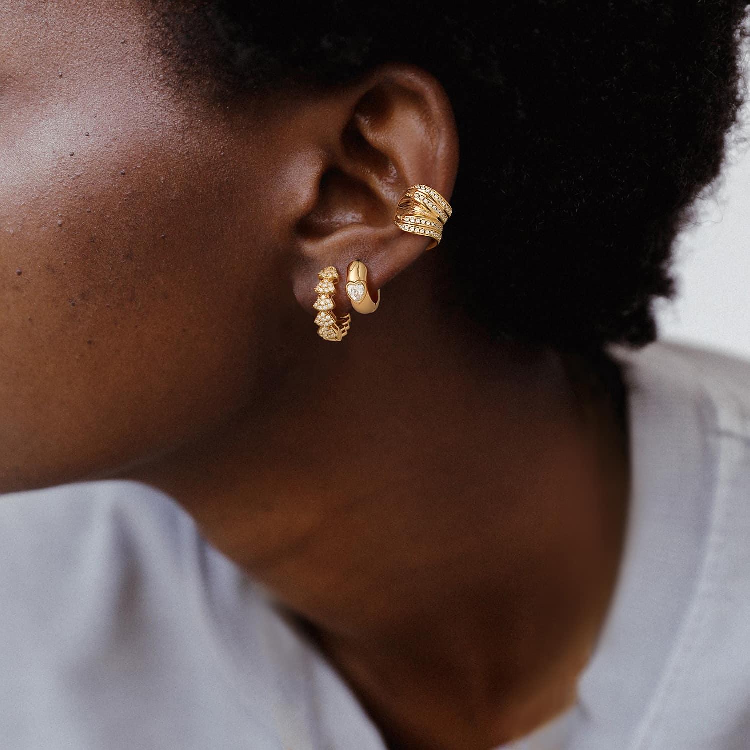 Close-up of a model wearing Myears® heart huggie hoop earrings with 14K gold details, heart-shaped women’s jewelry with a modern minimalist style.