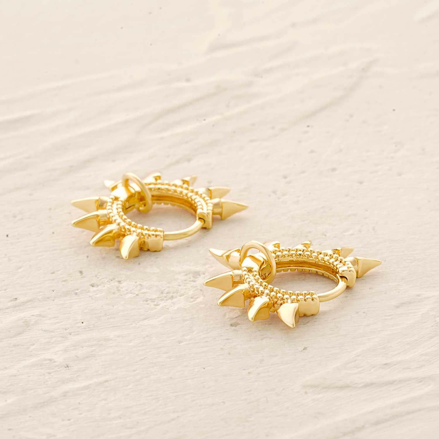 Close-up of spike huggie hoop earrings showing gold finish and spike design, jewelry details